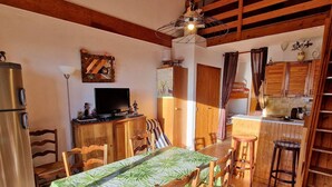 A compact kitchen with wooden cabinets, a dining area with a table and chairs, a refrigerator, and a television. - Central apartment, pets allowed - 6 guests (Saint-Michel-de-Chaillol)