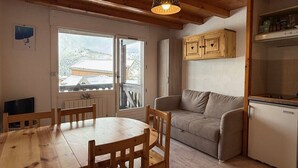 Ein gemütliches Zimmer mit einem Holzesstisch und Stühlen, einer Couch, einem Kühlschrank und einem Fenster mit Blick auf schneebedeckte Gebäude.