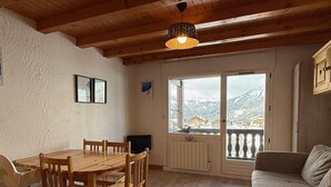 Ein gemütliches Zimmer mit einem Holzespeisetisch und Stühlen, einer Couch und einem großen Fenster mit Blick auf schneebedeckte Berge.