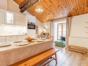A kitchen with white cabinets, a wooden ceiling, and a dining area with a table set for four. - Charming apartment in the village center, 6 ppl, near ski lifts (Aussois)