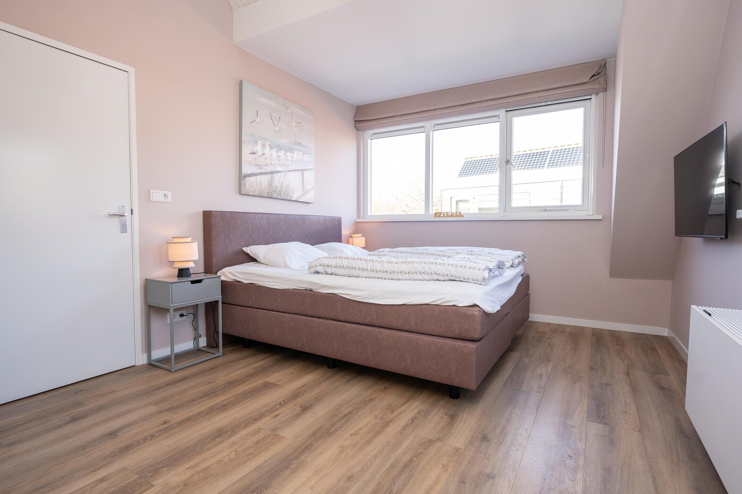 Un dormitorio con cama, lámparas de noche, ventana, televisor y puerta.