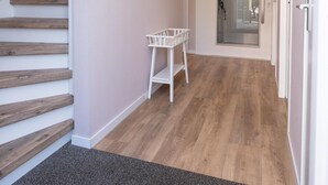 A hallway with a staircase, a white chair, and a door leading to an outdoor area. - Luxury, Peace and Space for the Whole Family (De Koog)