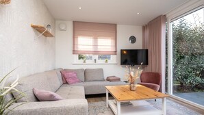 A modern living room with a sofa, a coffee table, a TV, and a window with curtains. - Luxury, Peace and Space for the Whole Family (De Koog)