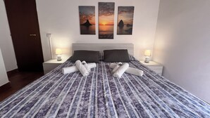 Ein ordentlich bezogenes Bett mit aufgerollten Handtüchern, einem Kopfteil und zwei Nachttischlampen.