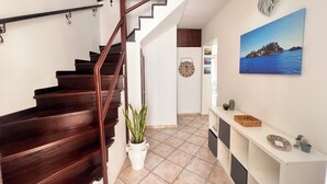 Eine Treppe mit Holzdielen und Metallgeländer, ein Blumentopf, eine Wanduhr, ein gerahmtes Bild und ein Konsolentisch mit Dekoration.