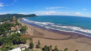 A coastal view with a beach, ocean, and buildings. - The Perfect Nest a Block Away to the Beach (Jacó)