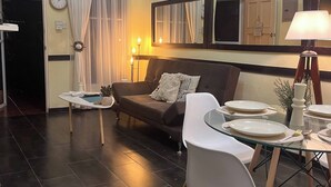 A living room with a sofa, dining table, chairs, a clock, and an air conditioning unit. - The Perfect Nest a Block Away to the Beach (Jacó)