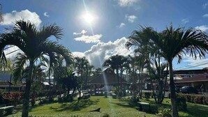 A sunny outdoor area with palm trees, a lawn, and a building in the background. - The Perfect Nest a Block Away to the Beach (Jacó)