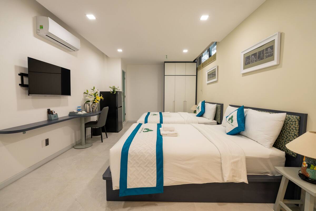 Une chambre d’hôtel avec deux lits, un bureau, une chaise, une télévision et un climatiseur fixé au mur.