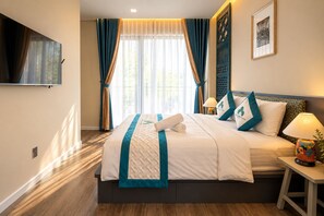 Ein Hotelzimmer mit Bett, Wandfernseher, einem Fenster mit Vorhängen und einem Wandbild.
