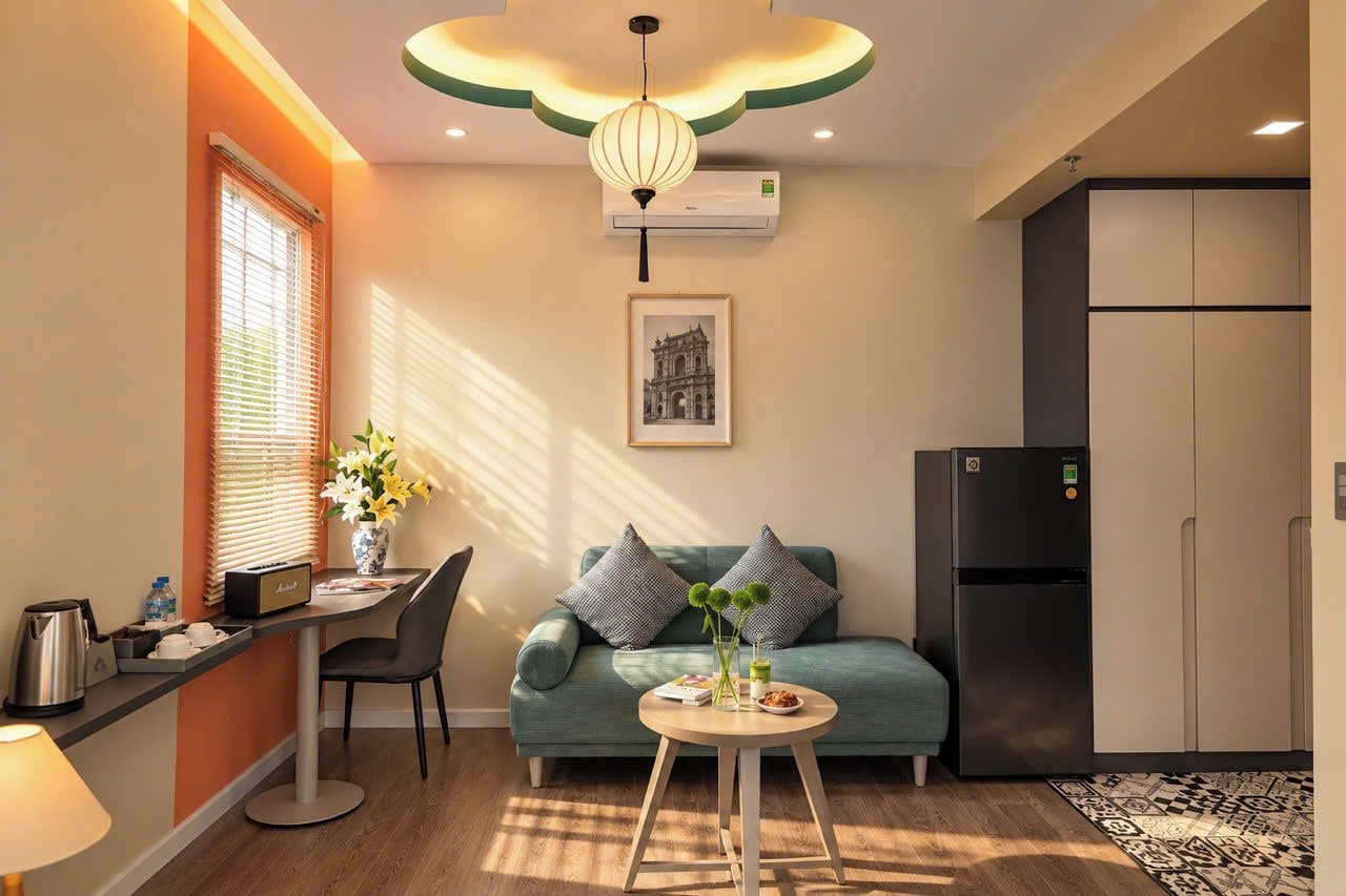 A modern kitchen with a refrigerator, a dining area with a table and chairs, and a sofa with decorative pillows.
