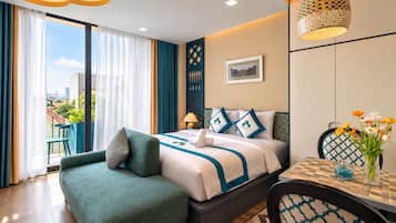 A hotel room with a bed, a sitting area with a chair, a dining table, and a view of the city through large windows.