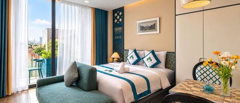 A hotel room with a bed, a sitting area with a chair, a dining table, and a view of the city through large windows.