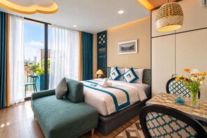 Une chambre d’hôtel comprenant un lit, un coin salon avec un fauteuil, une table à manger et une vue sur la ville grâce à de grandes fenêtres.
