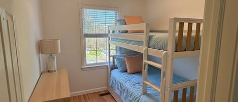 A room with bunk beds, a window with blinds, a lamp on a bedside table, and a door.