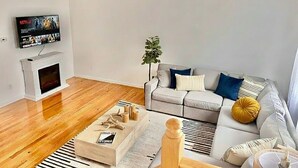 Un saló modern amb un sofà gris, una televisió de pantalla plana penjada a la paret, una llar de foc i una planta petita.