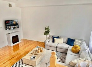 Ein modernes Wohnzimmer mit grauem Sofa, einem flachbildfernseher an der Wand, einem Kamin und einer kleinen Pflanze.