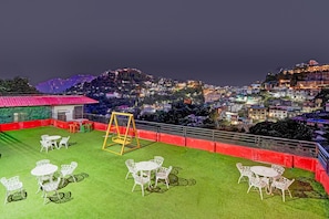 Terraço no telhado com mesas, cadeiras, balanço e vista para a cidade iluminada à noite.