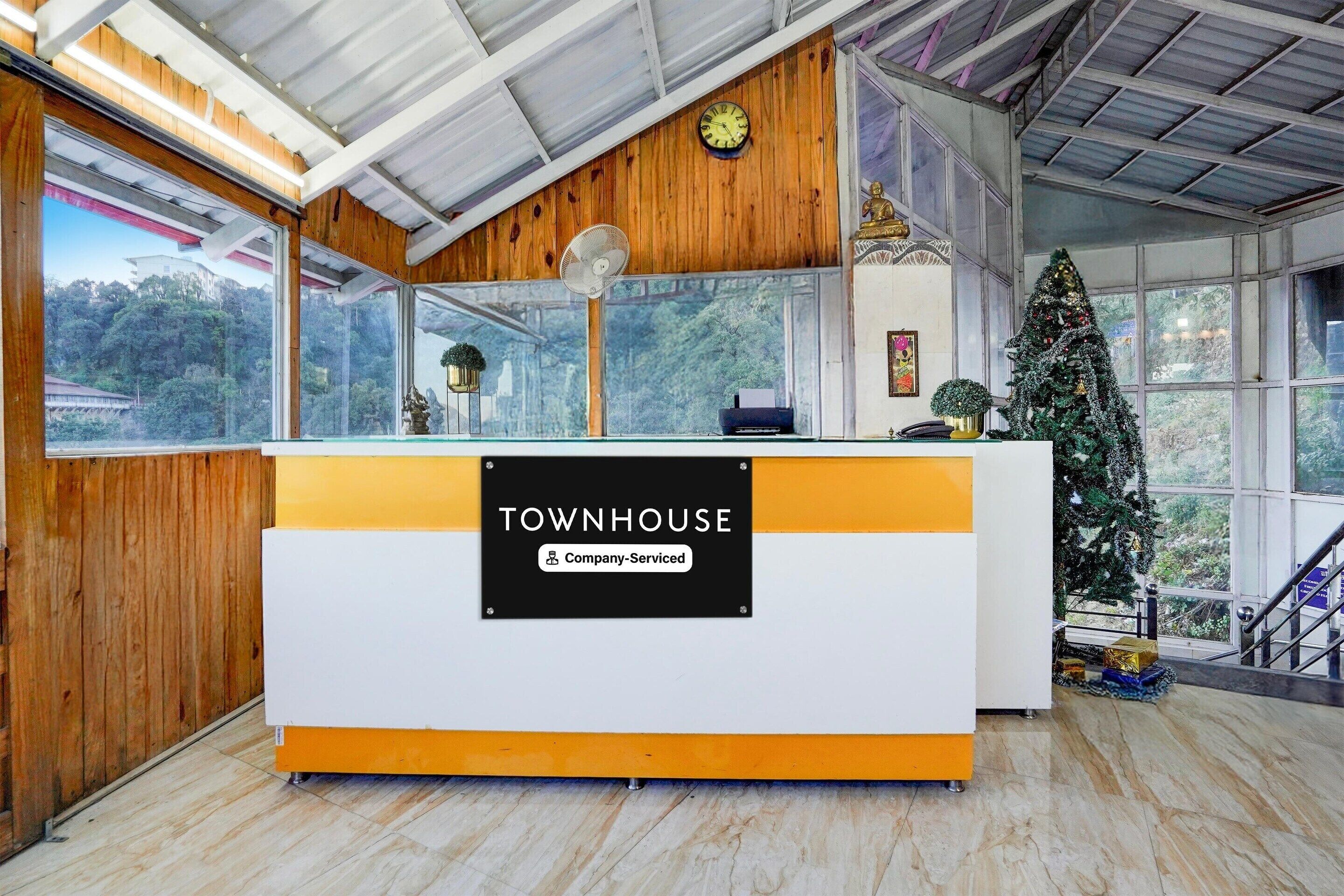 A reception desk with a sign reading 'TOWNHOUSE Company-Serviced,' a clock, a fan, and a Christmas tree.