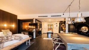 Una habitación de hotel moderna con cama, zona de comedor, televisor y chimenea.