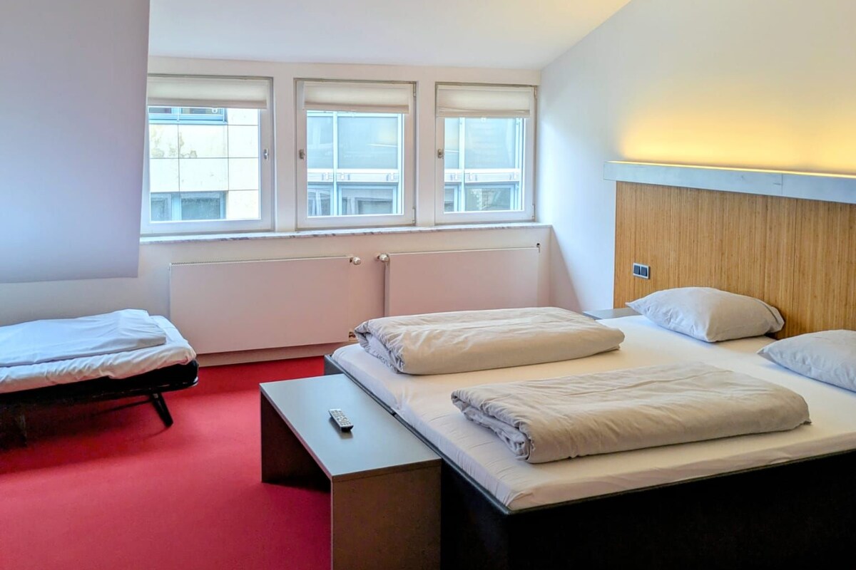 Una habitación de hotel con una cama grande, una cama más pequeña, un escritorio y una ventana con vistas.