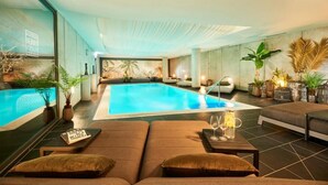 Una piscina interior con zonas de descanso, plantas en macetas y un mural en la pared.
