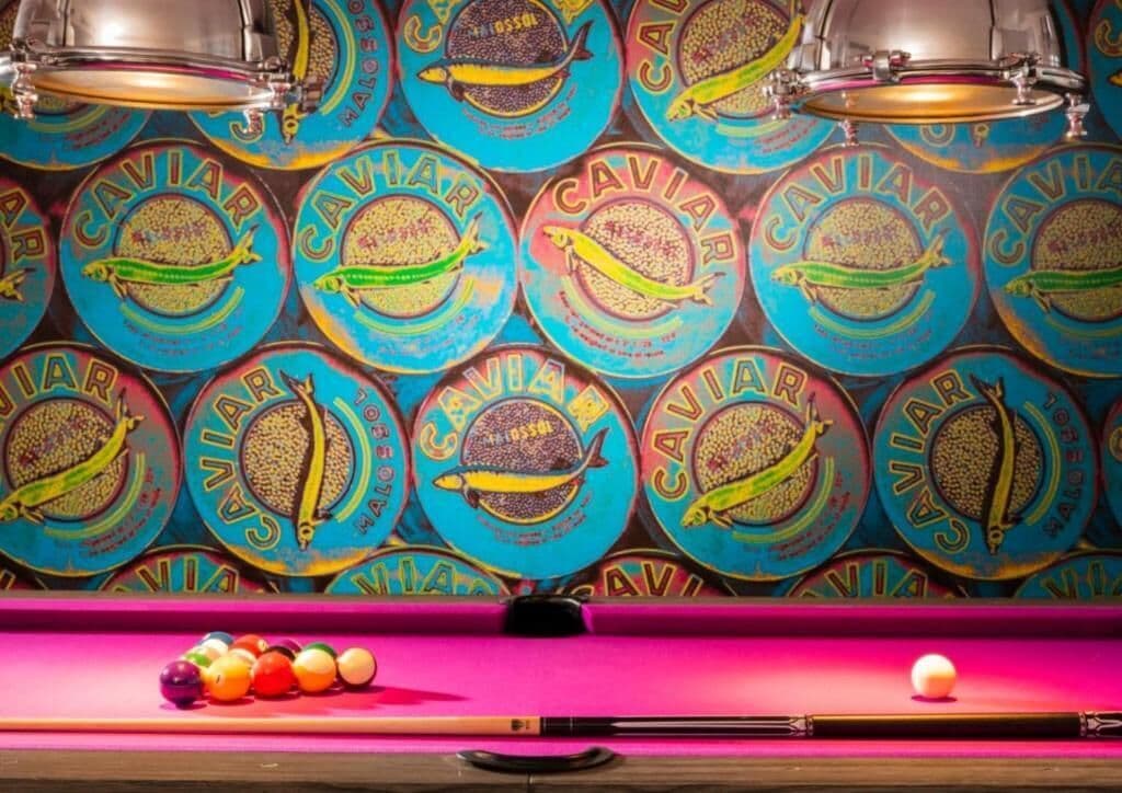 Una mesa de billar con bolas de colores y una taco, frente a una pared con diseños circulares.