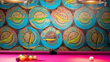 Una mesa de billar con bolas de colores y una taco, frente a una pared con diseños circulares.