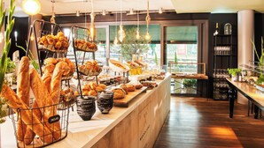 Zona de buffet con panes y pasteles variados, luces colgantes y vista al exterior.