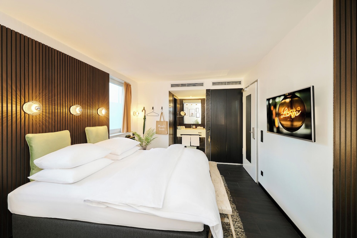 Una habitación de hotel moderna con una cama grande, un panel decorativo de madera, un espejo y un letrero de neón.