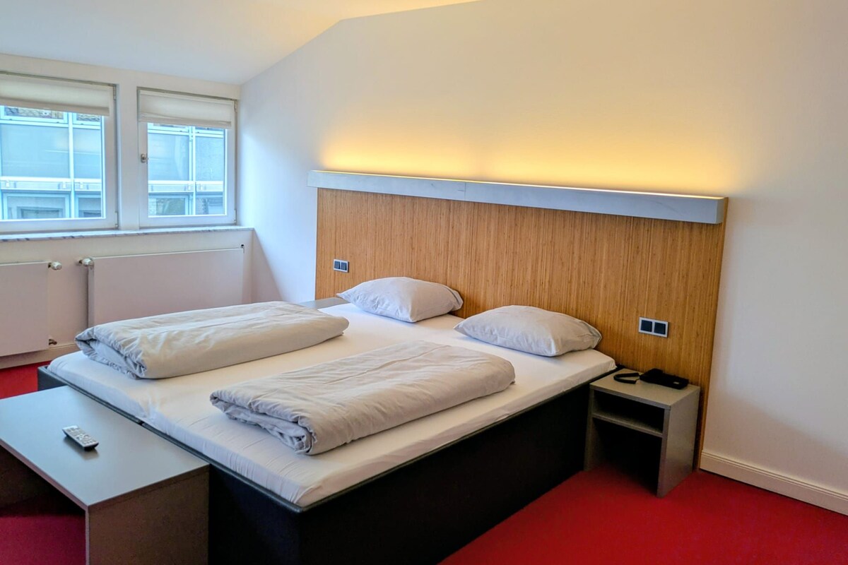 Una habitación de hotel con cama, mesita de noche y ventana.