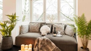 Una habitación acogedora con un ventanal grande, un sofá con cojines, una planta en maceta y un candelabro.