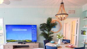 Een eetruimte met een televisie, een kroonluchter, een plant en een tafel gedekt voor vier personen.