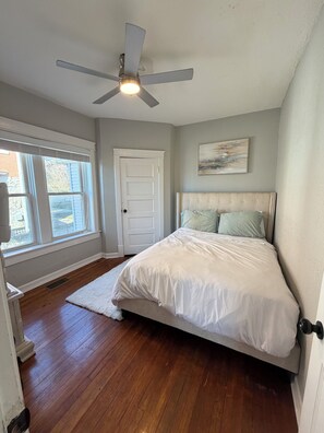 Une chambre à coucher avec un lit, un ventilateur de plafond, une fenêtre et une porte.