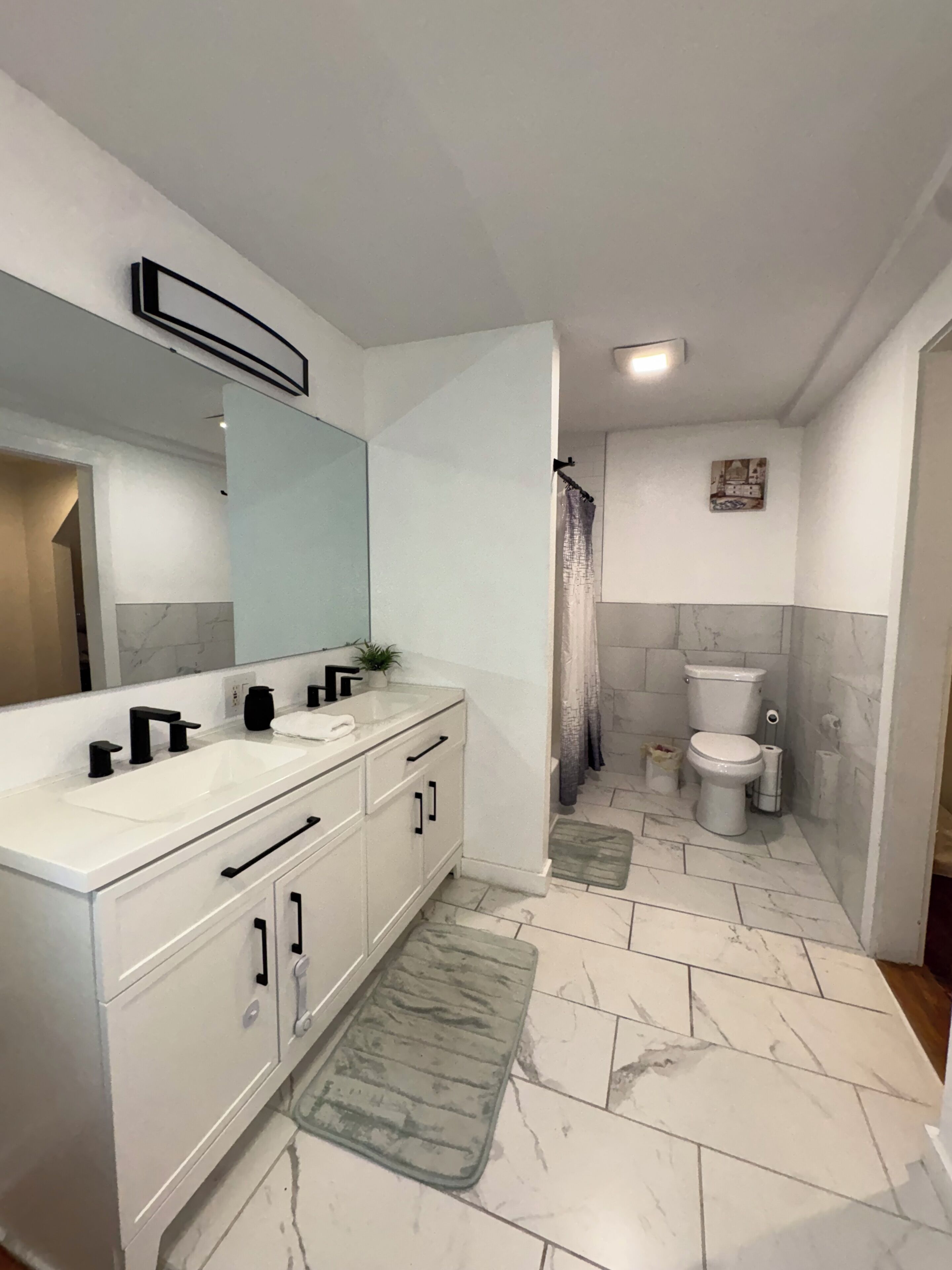 A bathroom with a white vanity, a large mirror, a toilet, and a shower area.