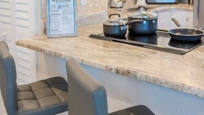Cozinha com bancada de mármore, dois banquetas de bar e utensílios de cozinha.