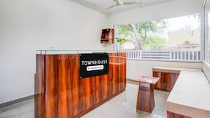 A reception desk with a sign reading 'TOWNHOUSE,' a glass partition, a ceiling fan, and a window with a view of trees. - Deluxe Hebbal Townhouse (Bengaluru)