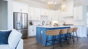 Una cocina moderna con armarios blancos, una isla azul, electrodomésticos de acero inoxidable y una araña.
