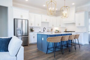 Una cocina moderna con armarios blancos, una isla azul, electrodomésticos de acero inoxidable y una araña.