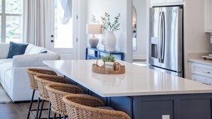 Una cocina moderna con una isla central, taburetes de bar, un refrigerador y un comedor con sofá.
