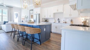 Una cocina moderna con armarios blancos, una isla central con taburetes y una araña.