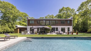 A modern two-story house with a swimming pool, outdoor seating, and a well-maintained lawn.