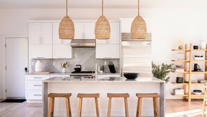 A modern kitchen with white cabinets, a marble countertop, wooden stools, and hanging wicker pendant lights.