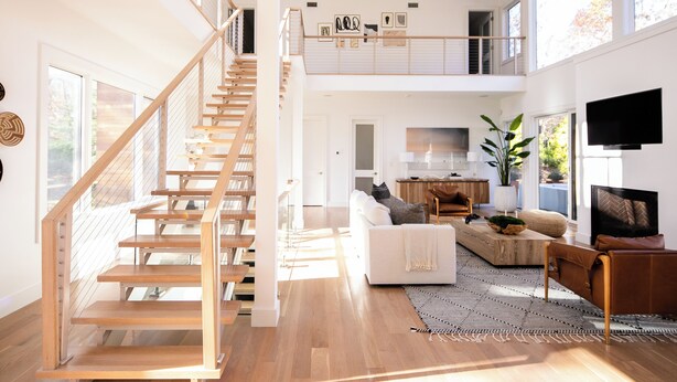 A spacious living area with a wooden staircase, a white sofa, a coffee table, and a TV.