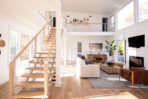 Amplia sala de estar con una escalera de madera, un sofá blanco, una mesa de centro y un televisor.