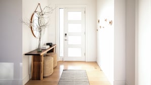 A hallway with a wooden console table, a vase with branches, a woven basket, a door with a frosted glass panel, and a hanging light fixture.