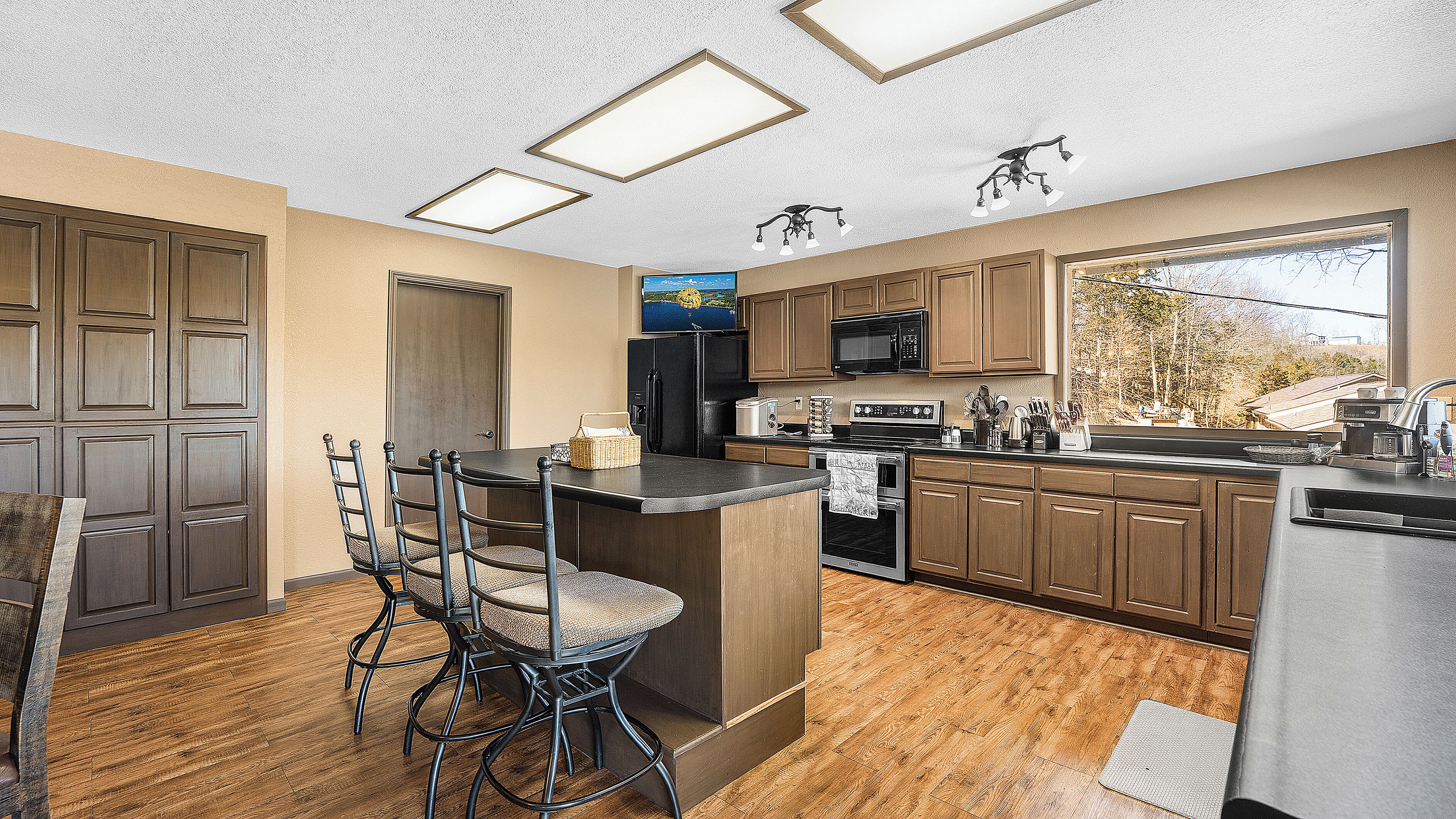 A kitchen with wooden cabinets, a central island, bar stools, a microwave, and a window with a view.
