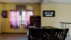 Quarto de hotel com uma mesa de jantar, duas cadeiras, uma cortina, um letreiro fixado na parede e um extintor de incêndio.