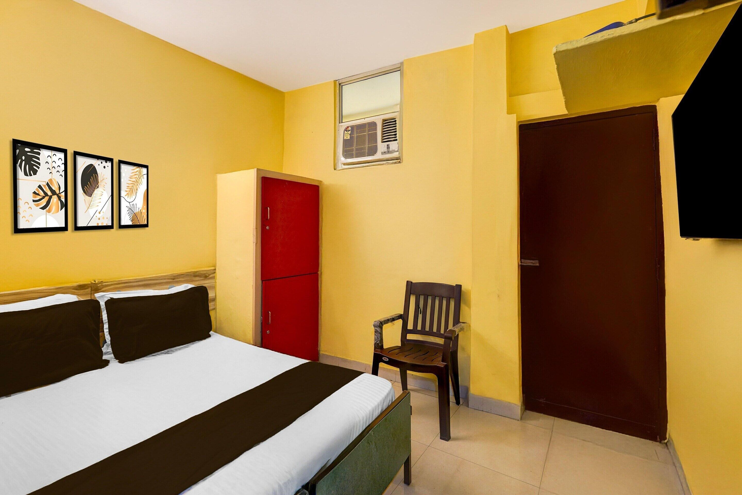 A room with a bed, a red wardrobe, a wooden chair, and framed artwork on the wall.