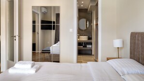 Ein Hotelzimmer mit einem Bett, einer Nachttischlampe, einem Spiegel und einem durch eine offene Tür einsehbaren Badezimmer.